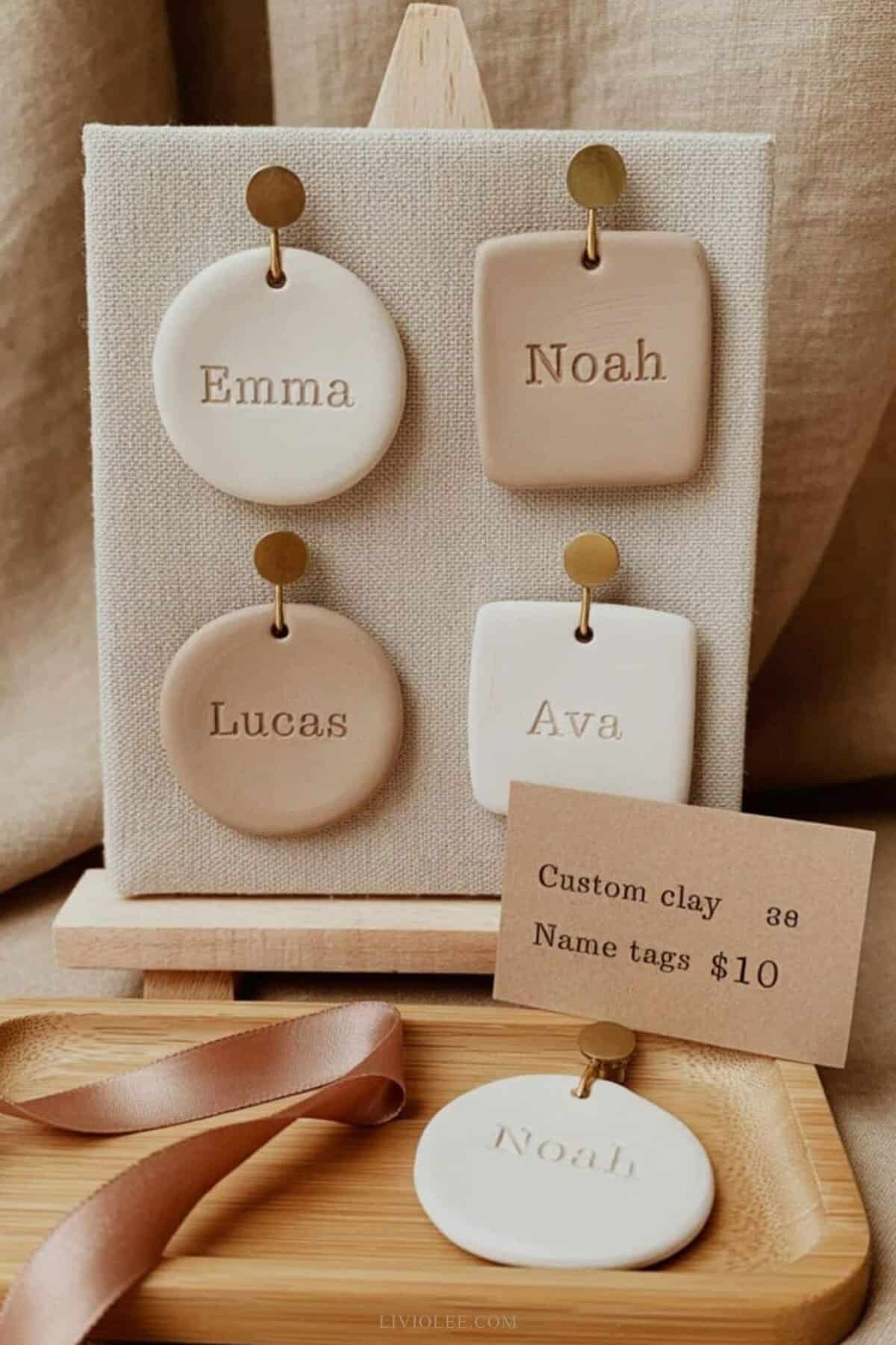 handmade clay name tags displayed at a craft market booth. Tags are simple circles and rectangles in soft white and sand-colored clay
