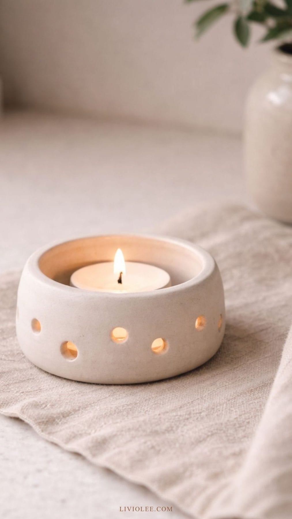 handmade clay tea light candle holder with a lit candle inside sitting on a linen placement