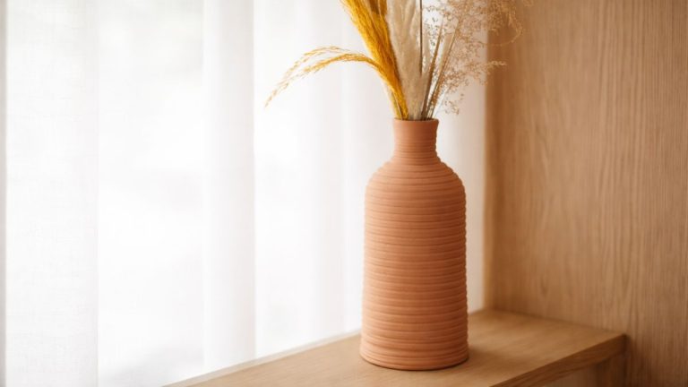 Air dry clay coil-built bottle vase with textured ridges, styled with dried grasses on a wooden shelf