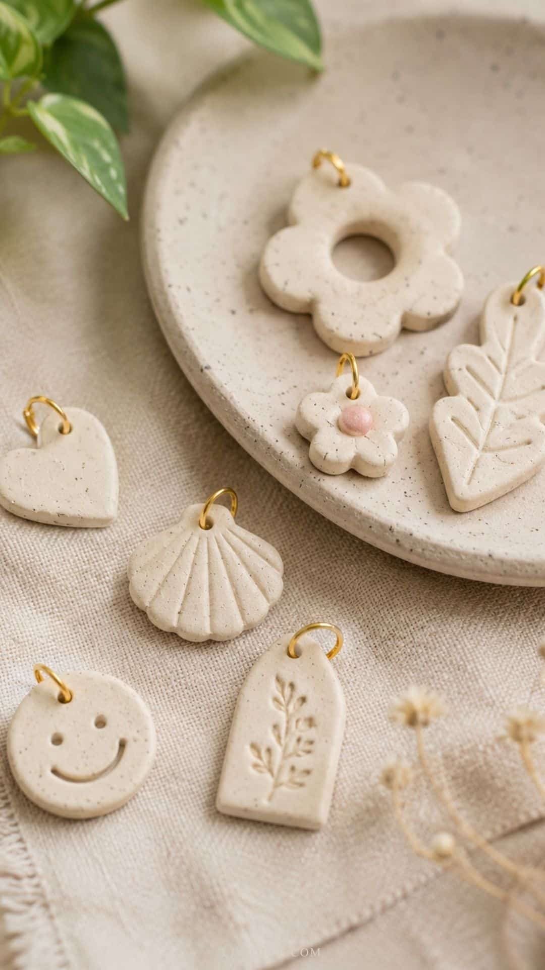 air dry clay charms in soft neutral tones arranged on beige linen fabric beside a ceramic dish