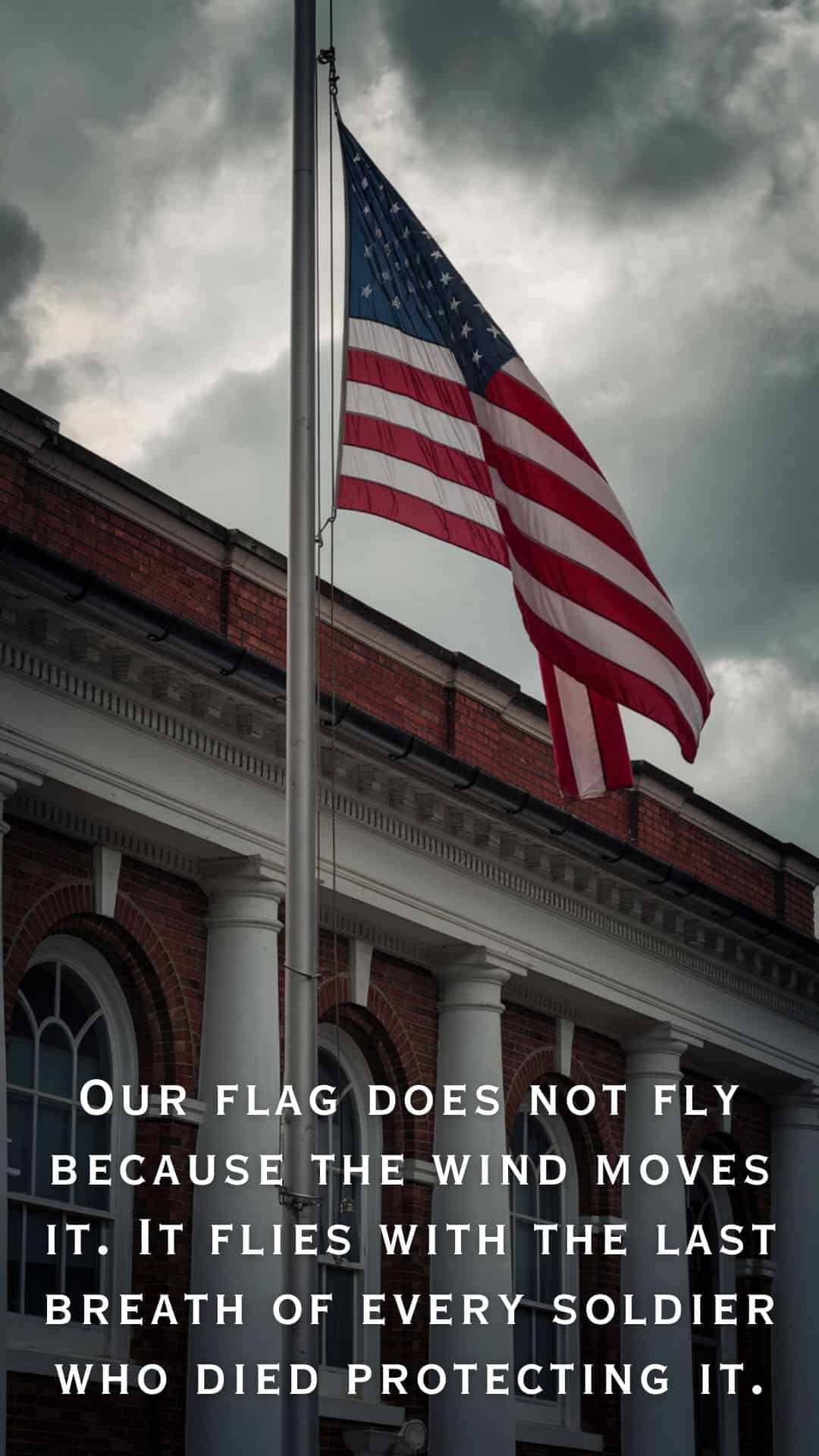Memorial Day image featuring an American flag flying at half-staff outside a historic building beneath dark storm clouds