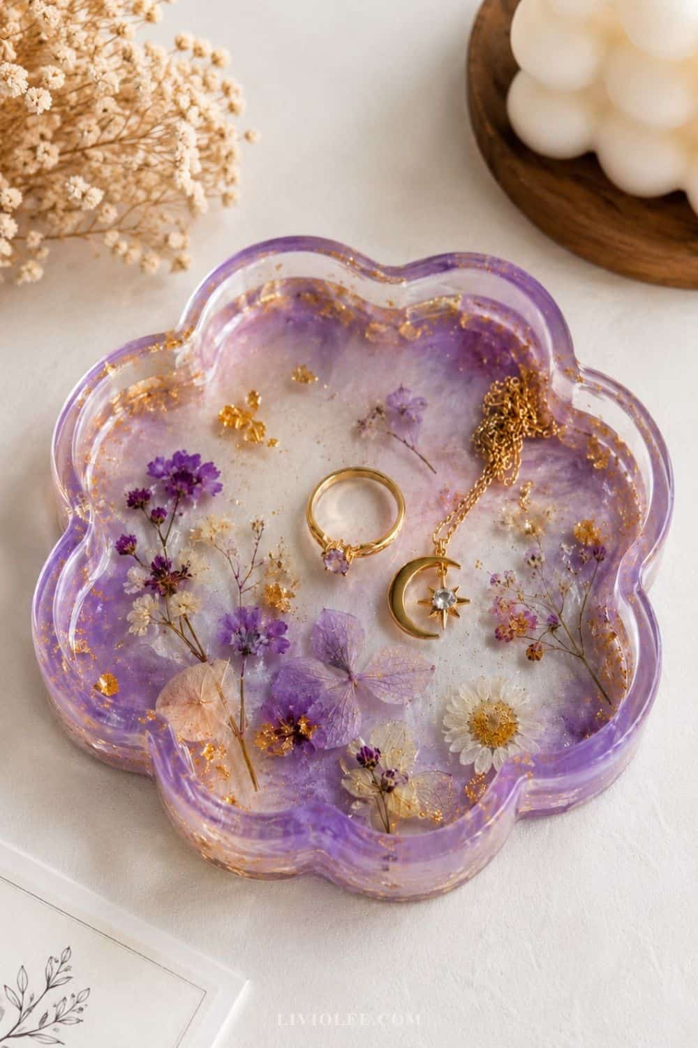 Handmade lavender resin trinket dish with pressed flowers and gold flakes, styled with delicate jewelry, dried florals, and a bubble candle in a soft neutral setting.