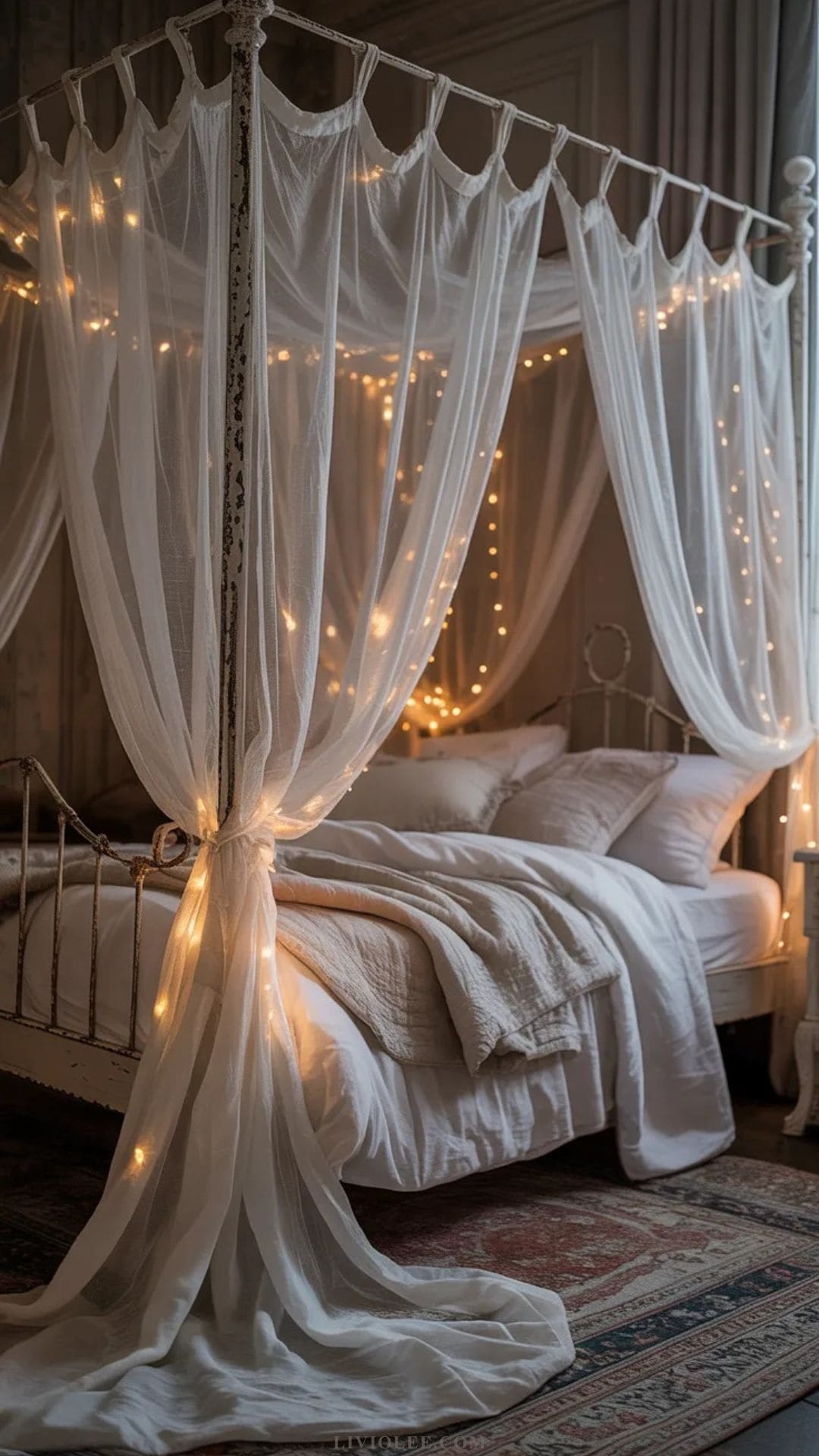 Romantic vintage canopy bed with sheer white draping and fairy lights in shabby chic bedroom