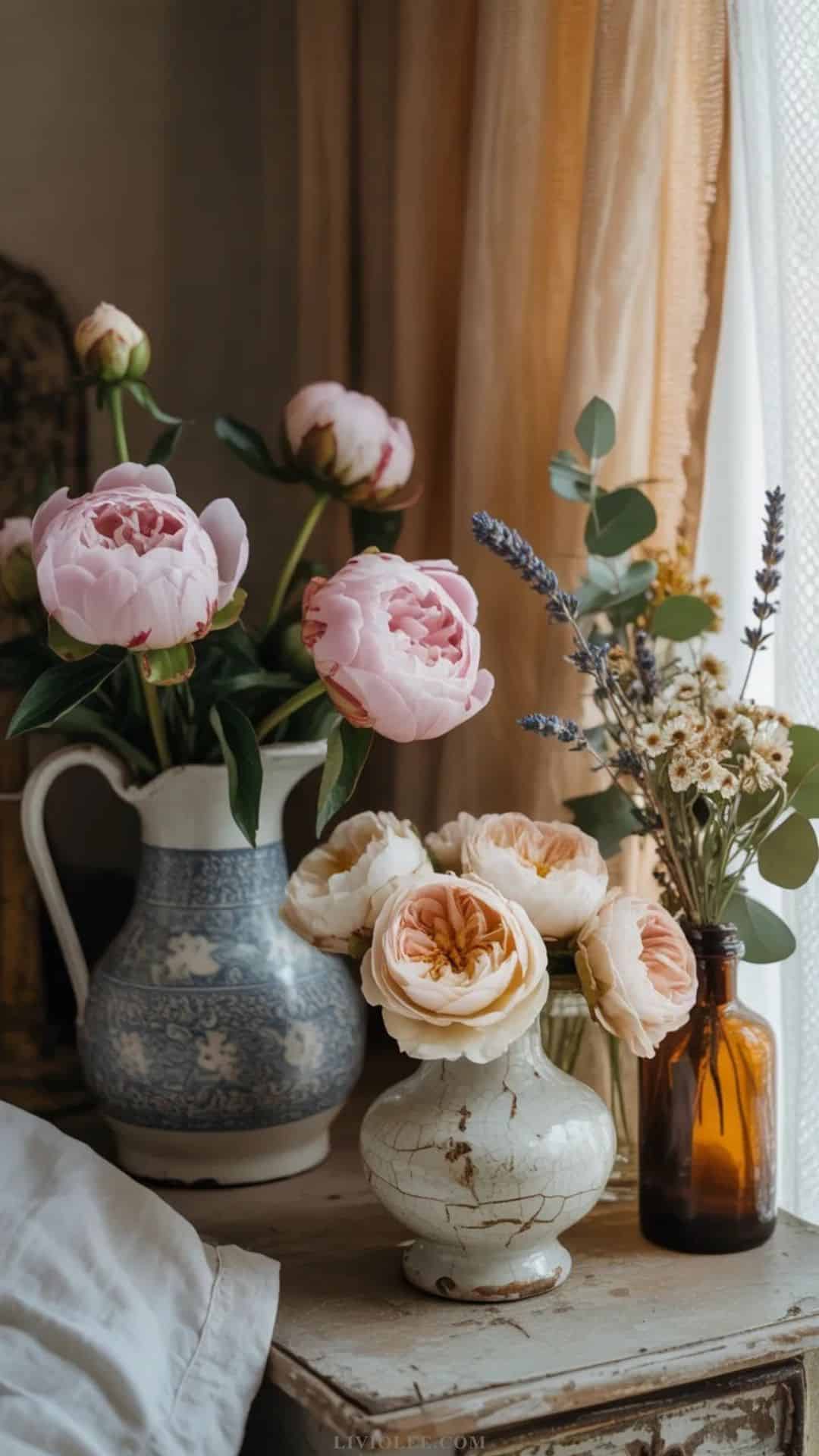 Fresh peonies and garden roses in a vintage ceramic jug in a shabby chic bedroom