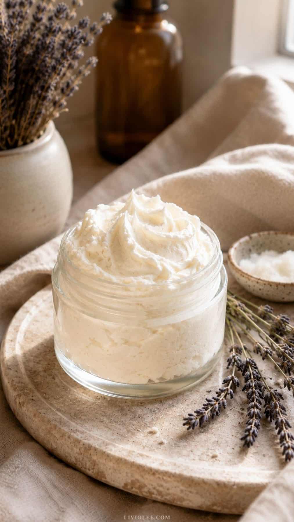 Glass jar of light whipped tallow lotion with an airy whipped texture styled on a stone tray with soft linen fabric, dried lavender, and warm natural light in a calm spa-inspired setting.